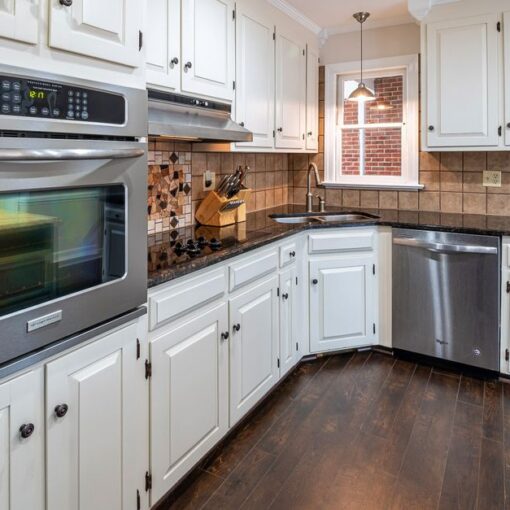 L-shaped kitchen with white cabinetry, stainless steel double oven, and dishwasher under dark granite countertops.