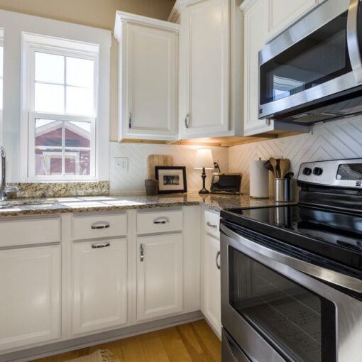 Bright white kitchen with granite countertops, stainless steel stove and microwave, and large windows above the sink.