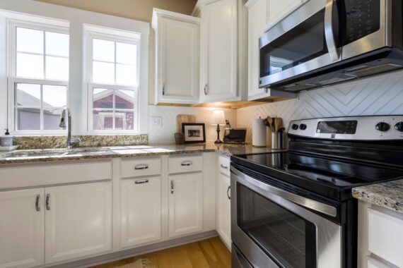 Bright white kitchen with granite countertops, white cabinets, and stainless steel stove and microwave by a double window over the sink.